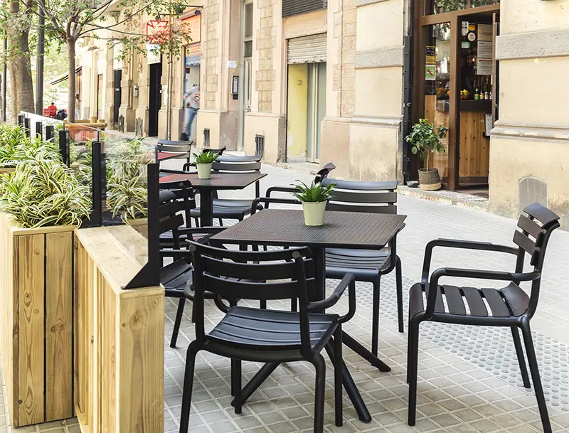 Uteservering på trottoar med svarta stapelbara stolar och fyrkantiga cafébord